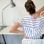 Overworked woman with back pain in office sitting on chair with bad posture